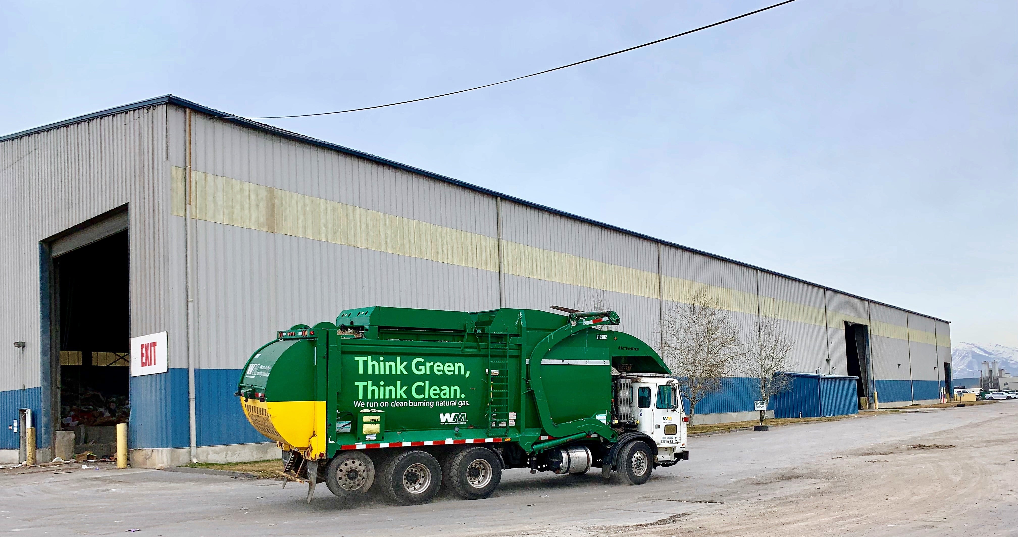 Photograph of Waste Management collection truck in front of MRF. The truck is green with text that reads "Think Green, Think Clean."