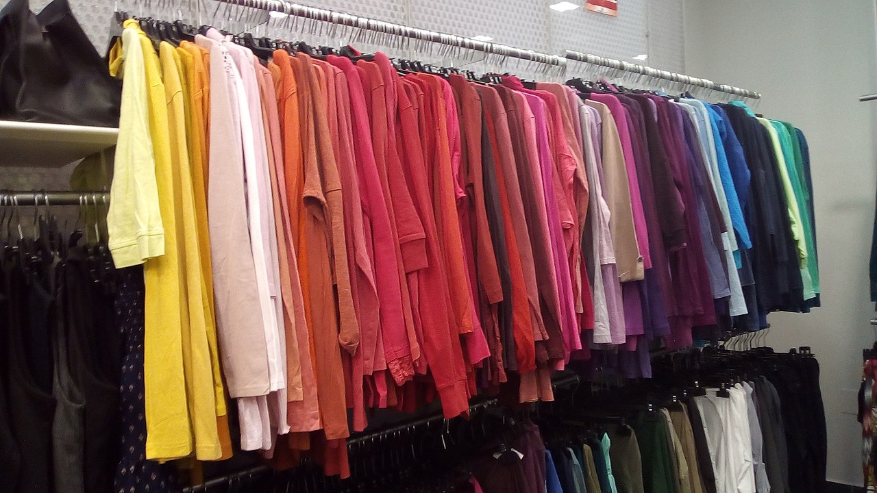 Photo of clothes on sales rack organized by color from yellow to green.