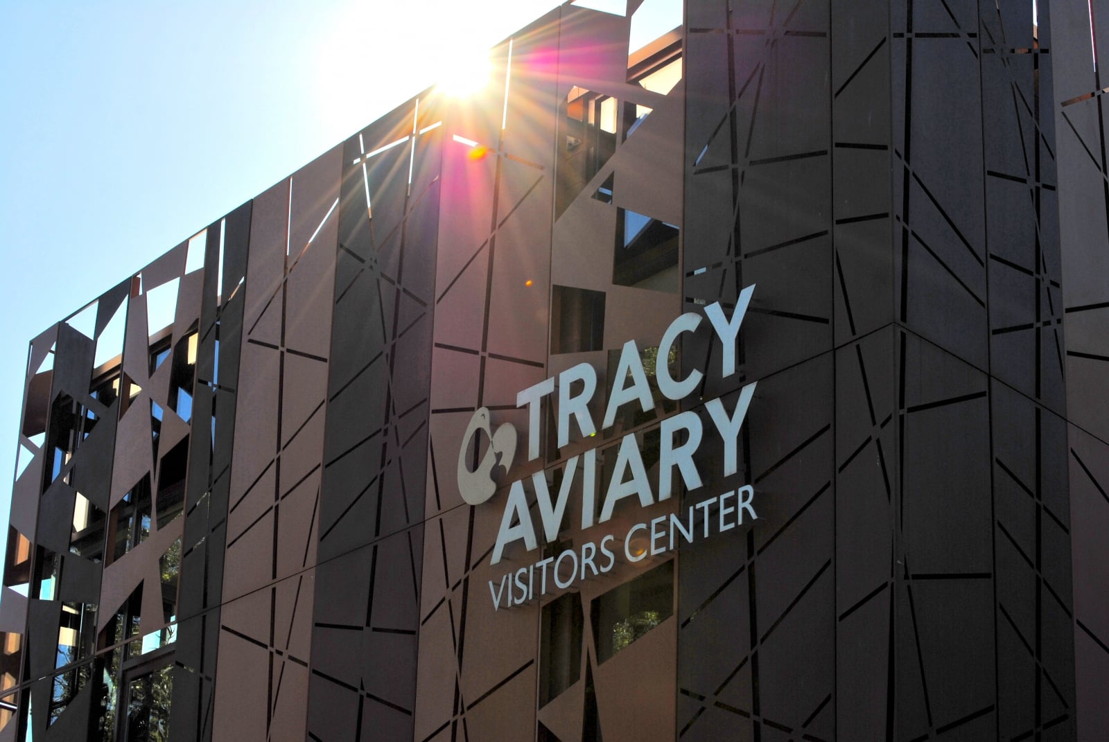 Photo of front of Tracy Aviary Visitors center with lights shining behind copper metal façade. 