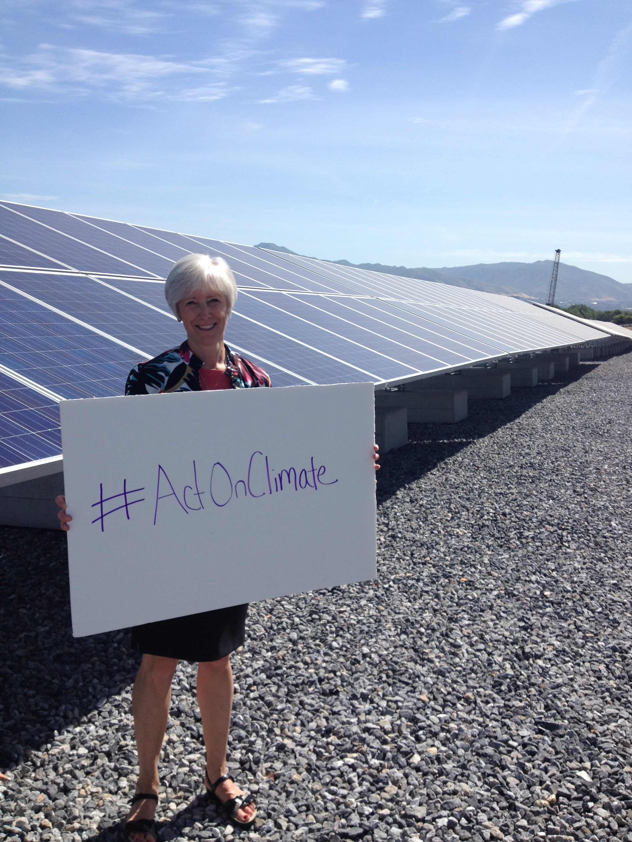 Photo of Vicki Bennett in front of solar panels with a sign reading #ActOnClimate.