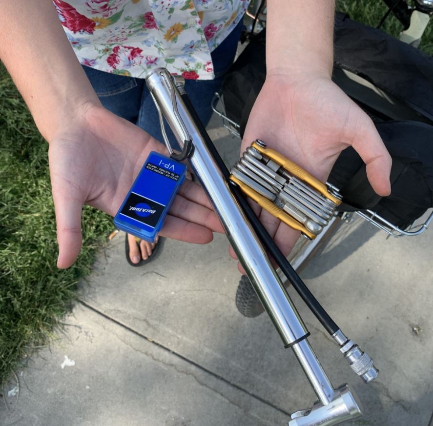 Hands holding a flat tire repair kit, bike pump and multitool.