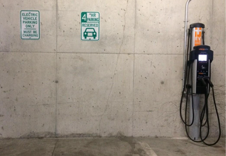 Electric vehicle charging station parking spots in concrete parking garage.